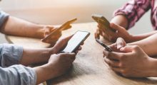 Group of friends playing app games in mobile phone and online together. Hands are holding smartphone circle on the table.