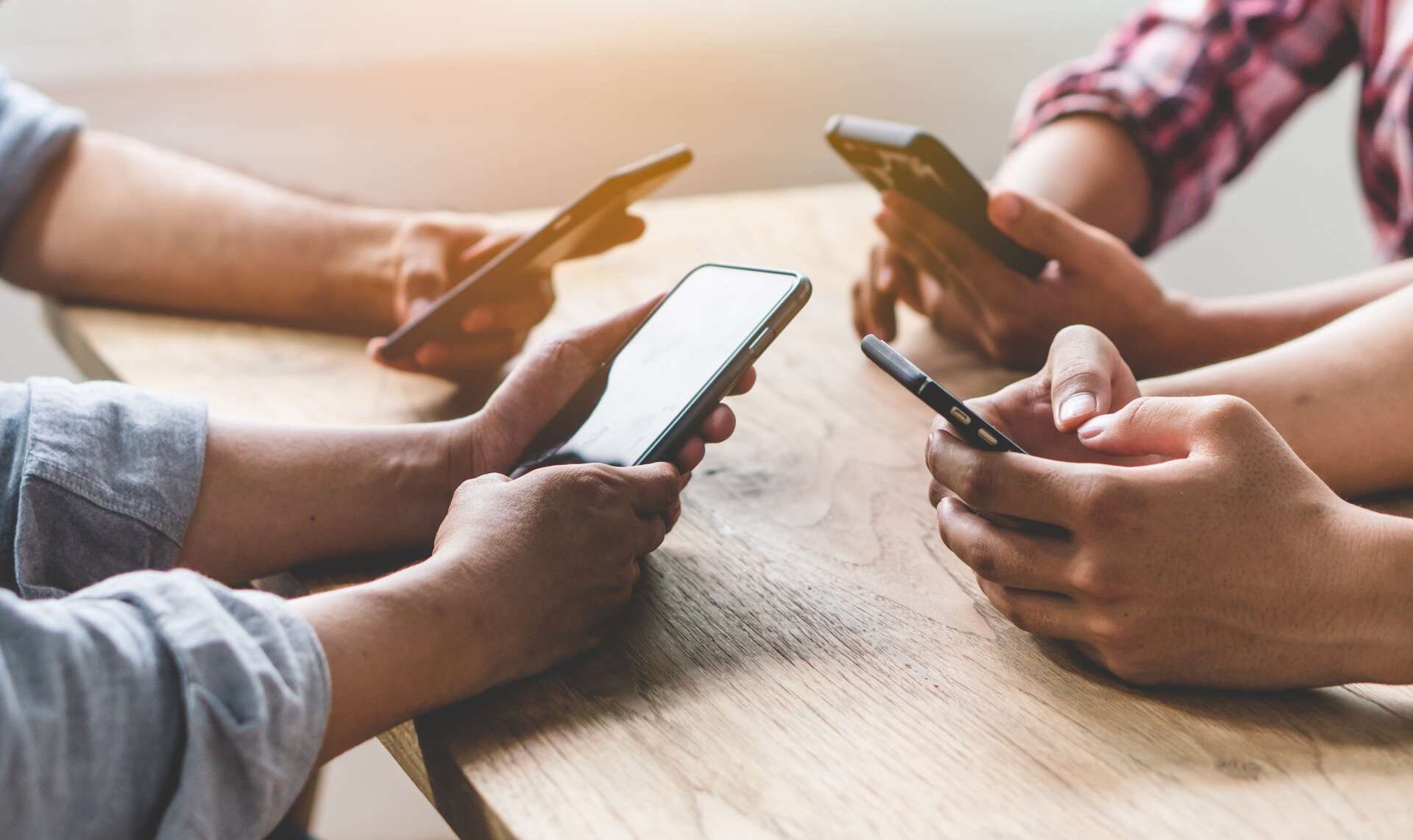 Group of friends playing app games in mobile phone and online together. Hands are holding smartphone circle on the table.